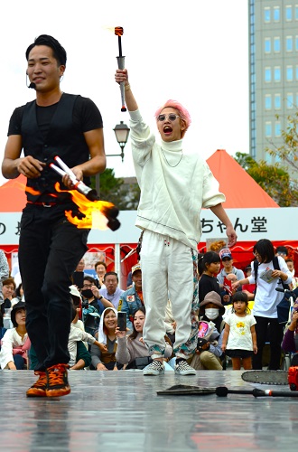 火のついた棒を投げるパフォーマンスに挑戦する観客
