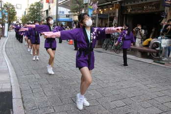 紫色の法被を着た女の子たちが通りで踊りを披露している