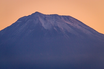 明け方のピンク色の空を背景に、うっすら雪化粧をした富士山頂の写真。