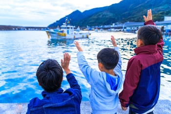 岸壁から漁船に手を振る子どもたち