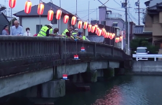 橋の上から灯篭を川に流す男性たち