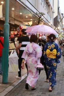 浴衣を着た女性が傘をさしながら、祭りを楽しむ様子