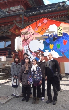 初詣の文字と富士山の絵が描かれた木の看板の前で記念撮影をする家族