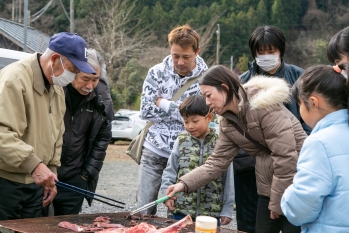 トングを使って、肉を焼く地域の方と祭りに訪れた家族