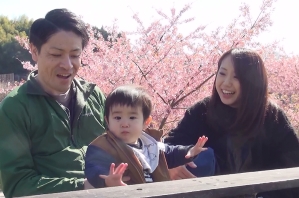 子どもを中心に桜の前でほほ笑む家族